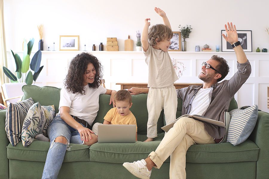 Client Center - Excited Family with Two Sons Sitting on the Couch Using a Laptop and Playing