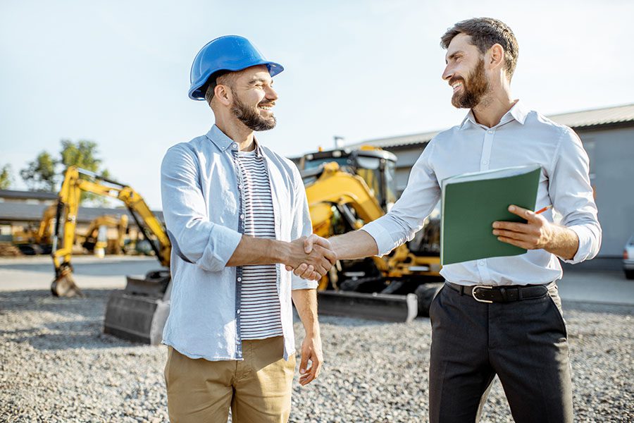 Specialized Business Insurance - Smiling Contractor and Businessman Shaking Hands at a Construction Jobsite with Heavy Machinery in the Background